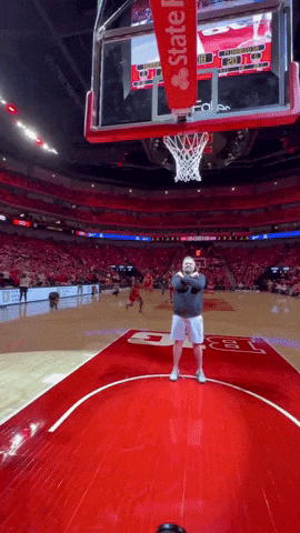 a man stands on a basketball court in front of a hoop that says state farm on it