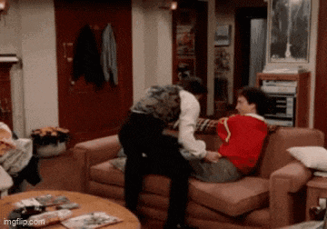 two men are sitting on a couch and one of them is wearing a red sweater