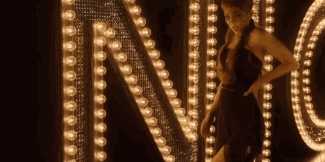 a woman in a black dress is standing in front of the letter n