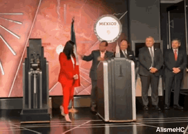 a woman in a red suit is standing in front of a podium with a sign that says mexico