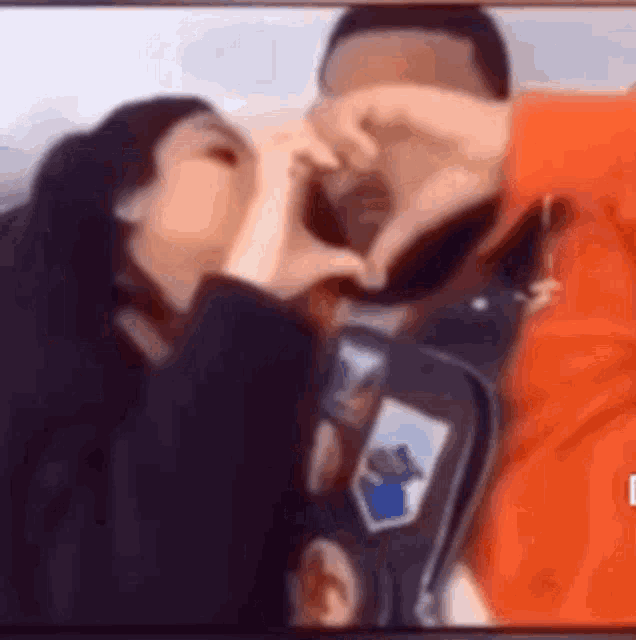 a man and a woman are kissing and making a heart shape with their hands .
