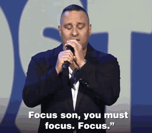 a man singing into a microphone with the words " focus son you must focus " behind him