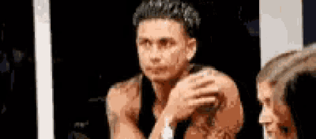 a shirtless man is sitting in front of a mirror with a woman behind him .