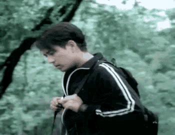 a man wearing a black jacket and a backpack is walking through the woods .