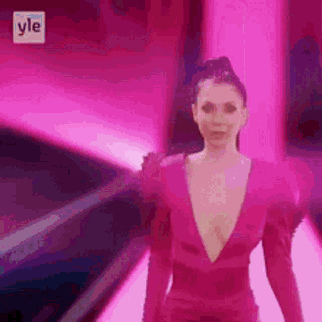 a woman in a pink dress with a plunging neckline is standing in front of a pink background .