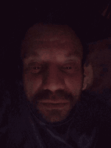 a man with a beard is smiling with his eyes closed in the dark