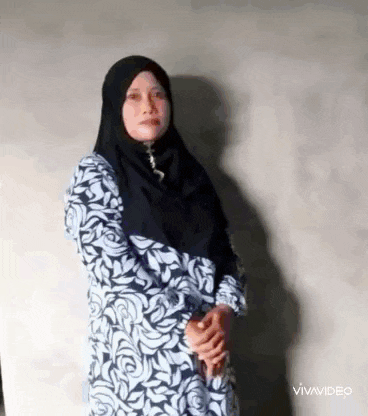 a woman in a hijab is standing in front of a wall .