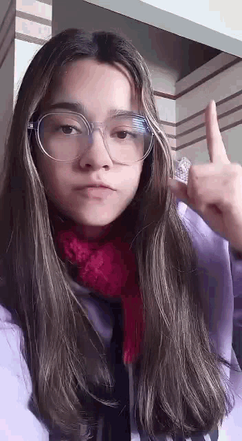 a young woman wearing glasses and a scarf is giving a middle finger .