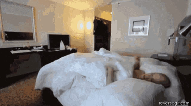a man is sleeping on a bed in a hotel room with the website reversegif.com visible in the corner