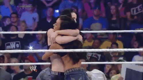 a woman is hugging another woman in a wrestling ring with a crowd watching .