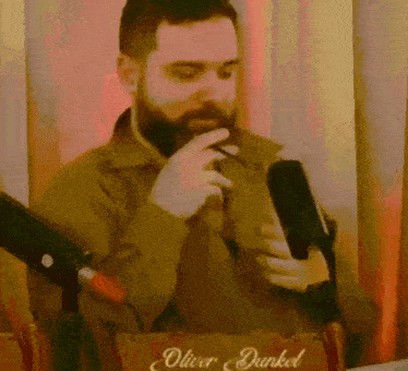a man with a beard is standing in front of a microphone and a sign that says oliver dunkel on it