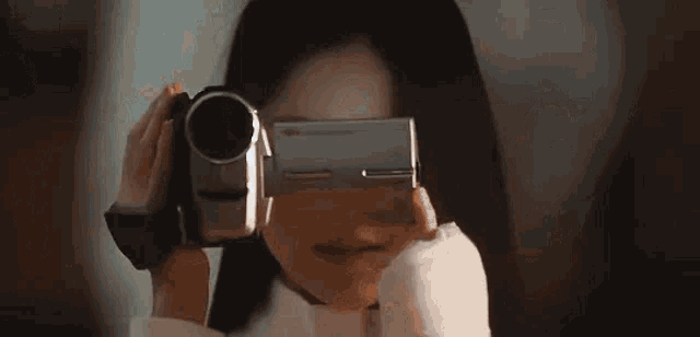 a woman is holding a video camera to her face .