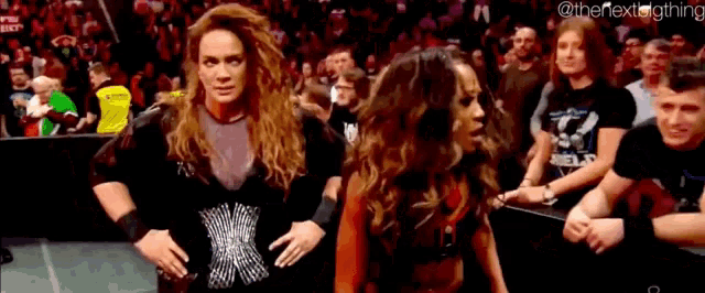 two women are standing next to each other in front of a crowd at a wrestling event .