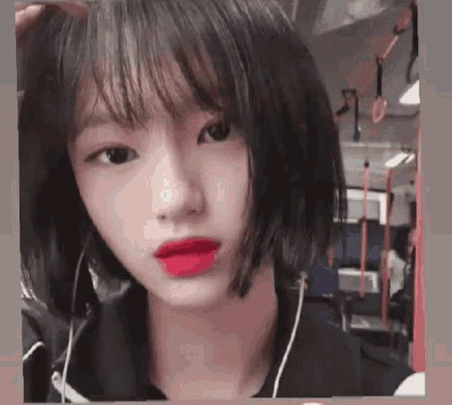 a girl with short hair and red lipstick is wearing headphones and looking at the camera .