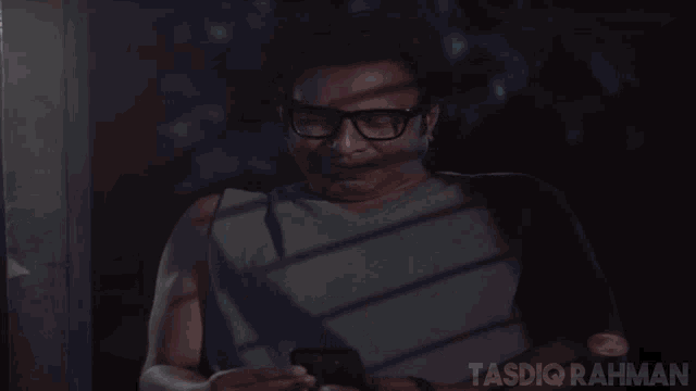 a man wearing glasses is looking at his phone and the words tasdi rahman are visible