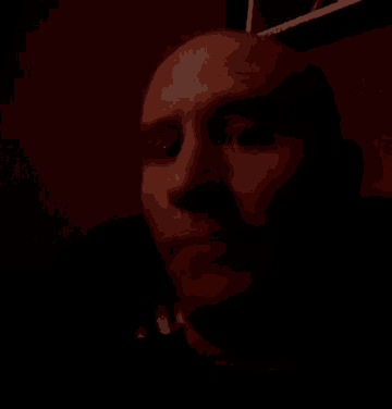 a man 's face is shown in a dark room with a picture of a man on the wall behind him