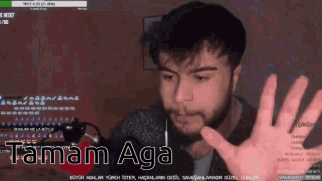 a man with a beard is waving his hand in front of a screen that says tamam aga on it