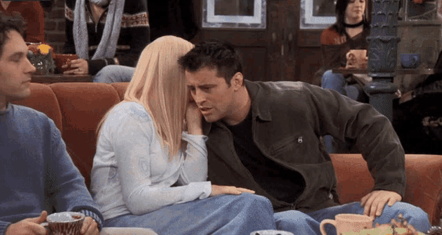 a man and a woman are sitting on a couch and the man is wearing a jacket with the letter e on it