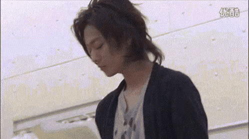 a young man with long hair is standing in front of a wall with his eyes closed .