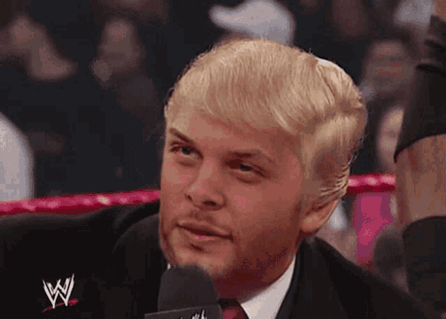 a man in a suit and tie is talking into a microphone while wearing a wig .