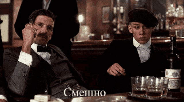 two men are sitting at a table with a bottle of whiskey and a tray of glasses with the word смешно on it