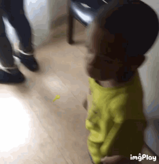 a little boy in a yellow shirt is standing on a wooden floor with a yellow key in the background ..