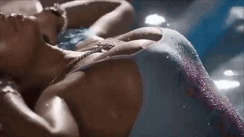 a woman in a mermaid costume is laying on her back in the water .