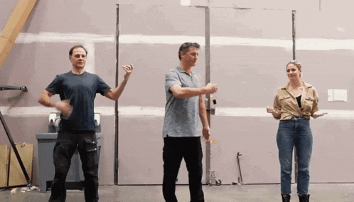 three people are dancing in a room in front of a wall .