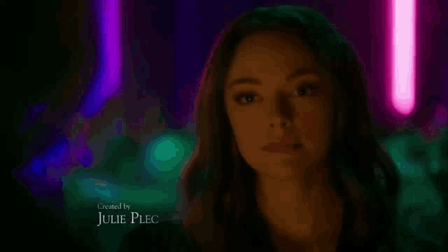 a woman is standing in a dark room with neon lights behind her .