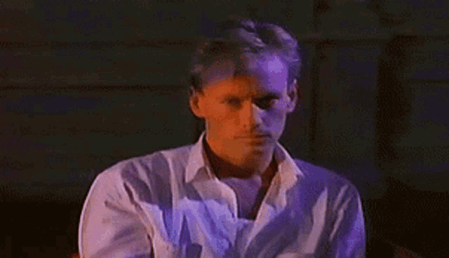 a man in a white shirt is standing in a dark room looking at the camera .