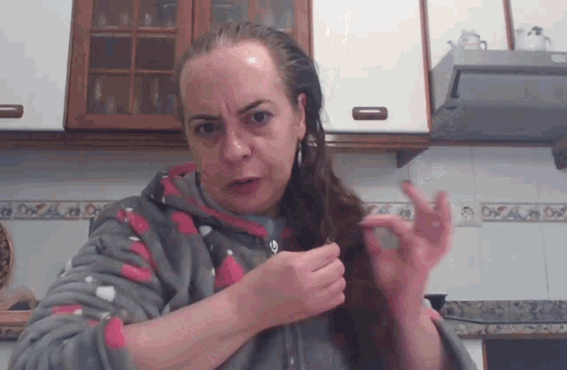 a woman in a kitchen with a hooded jacket on is holding her hair in a ponytail