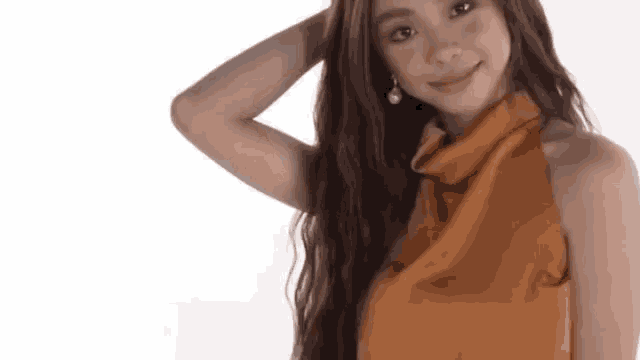 a woman with long hair is wearing a brown top and earrings .