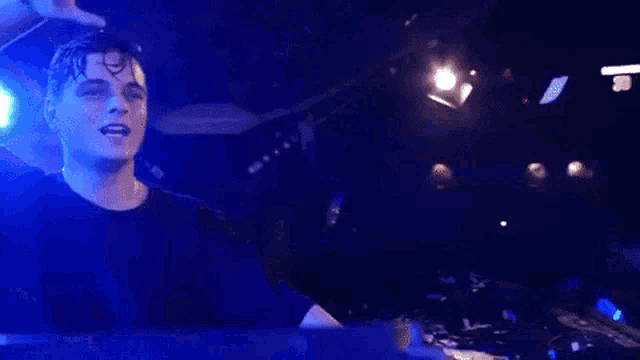 a young man in a black shirt is standing in front of a blue light .