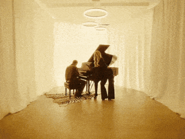 a man sits at a piano while a woman stands behind it