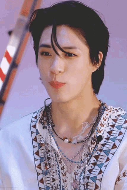 a close up of a man wearing a necklace and a white shirt