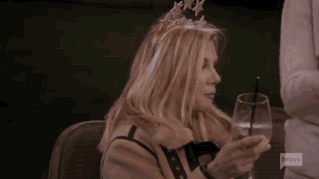 a woman wearing a tiara is holding a glass of wine and a straw .
