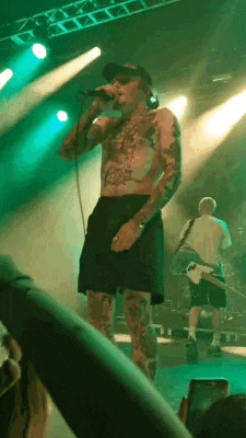 a man without a shirt is singing into a microphone on stage .
