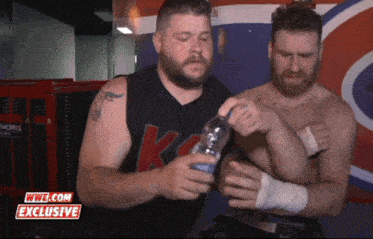 two men are holding a bottle of water in front of a wwe.com exclusive banner