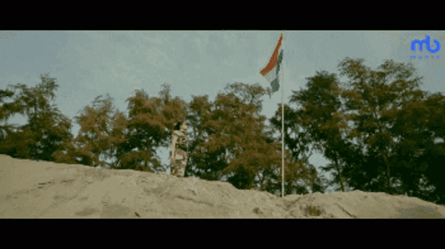 a man stands on top of a sandy hill next to a flag pole