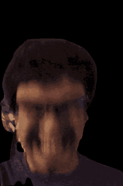 a man with glasses and a beard is smiling in a dark room