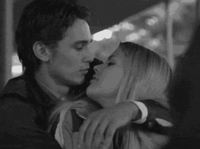 a black and white photo of a man and a woman hugging each other .