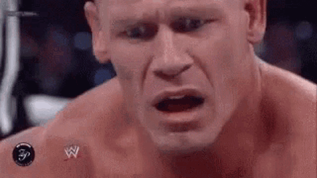 a close up of a man 's face with his mouth open and a wrestling logo on his chest .