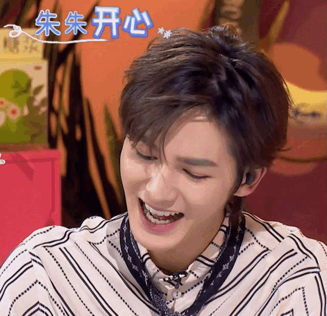 a man in a striped shirt is laughing in front of a pink box with chinese writing on it