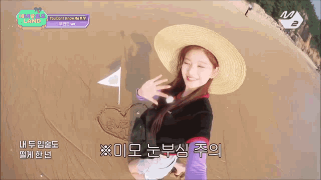 a girl wearing a straw hat is standing on a beach with a heart drawn in the sand