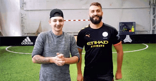 a man wearing an etihad airways jersey shakes hands with another man on a soccer field