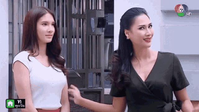 two women are standing next to each other in front of a building and one of them is smiling