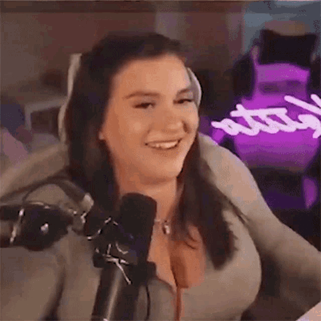 a woman is smiling while sitting in front of a microphone in a room .