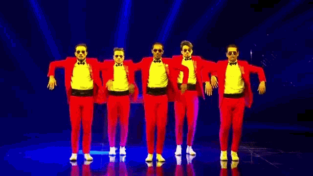 a group of men in red suits are dancing on a stage .