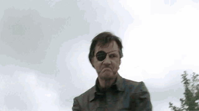 a man wearing a bandage on his eye is standing in front of a cloudy sky .