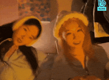 two women wearing knitted hats are standing next to each other in front of a sign that says vlive